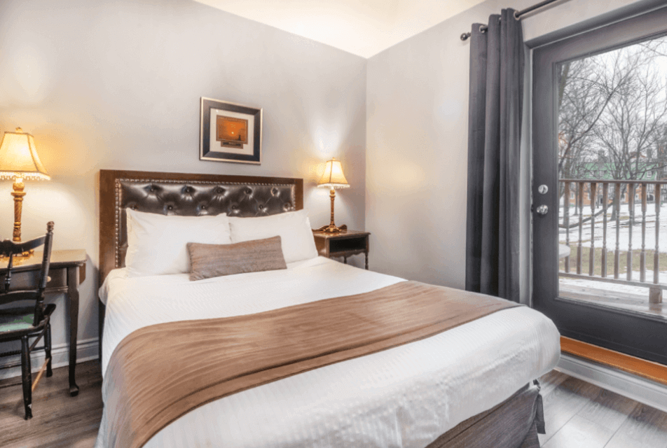 Acadia Hotel Quebec City – chambre Queen avec porte-fenêtre et balcon, éclairage chaleureux et vue hivernale