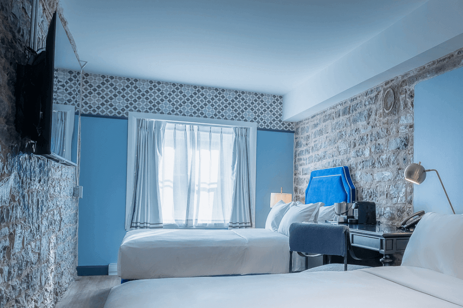 Acadia Hotel Quebec City double room with exposed stone wall, blue accents, desk and wall-mounted TV