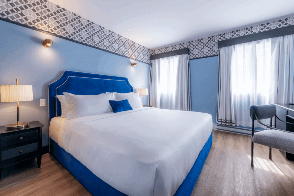 Acadia Hotel Quebec City guest room with blue headboard, bright windows and workspace