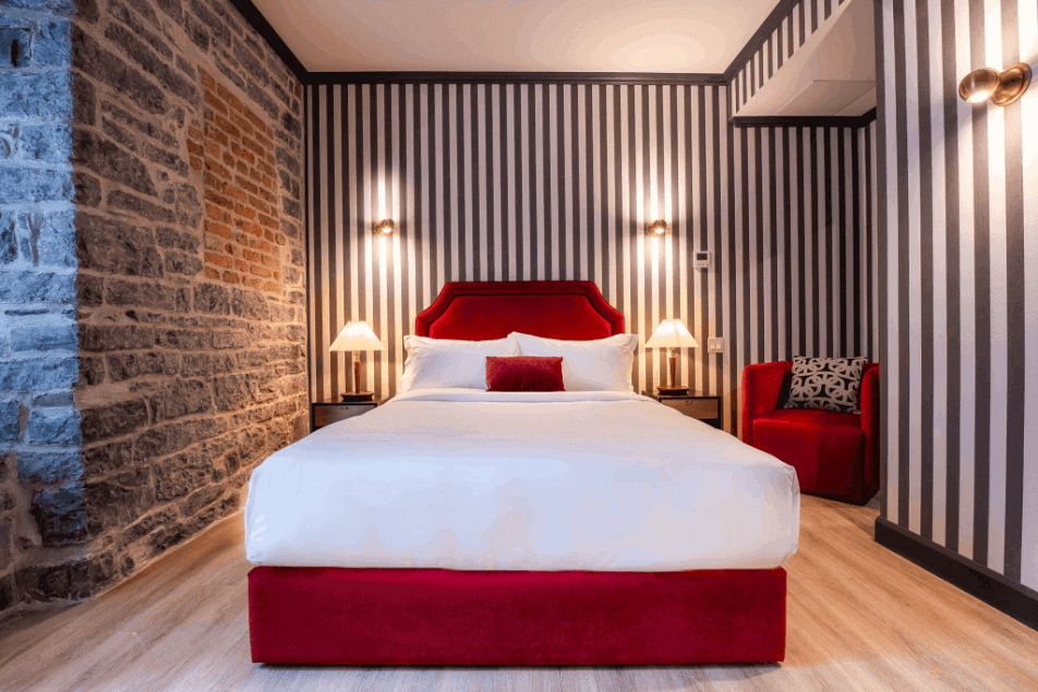 Acadia Hotel Quebec City guest room with red headboard, stone wall and striped wallpaper